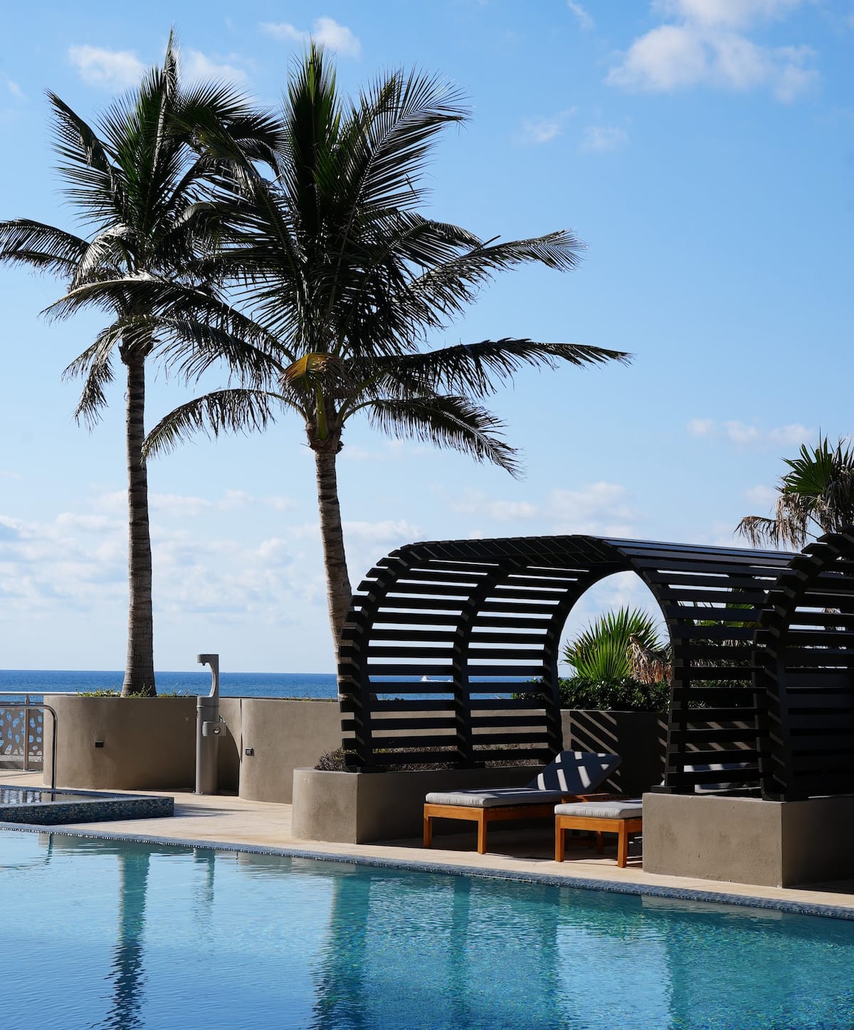 A curved beach pergola and cabanas among palms by the pool