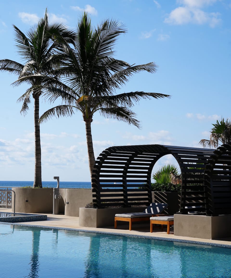 A curved beach pergola and cabanas among palms by the pool