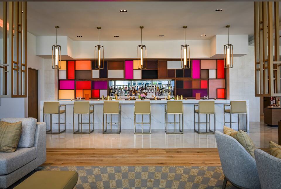 A resort bar with warm backlit shelving and ocean-view seating