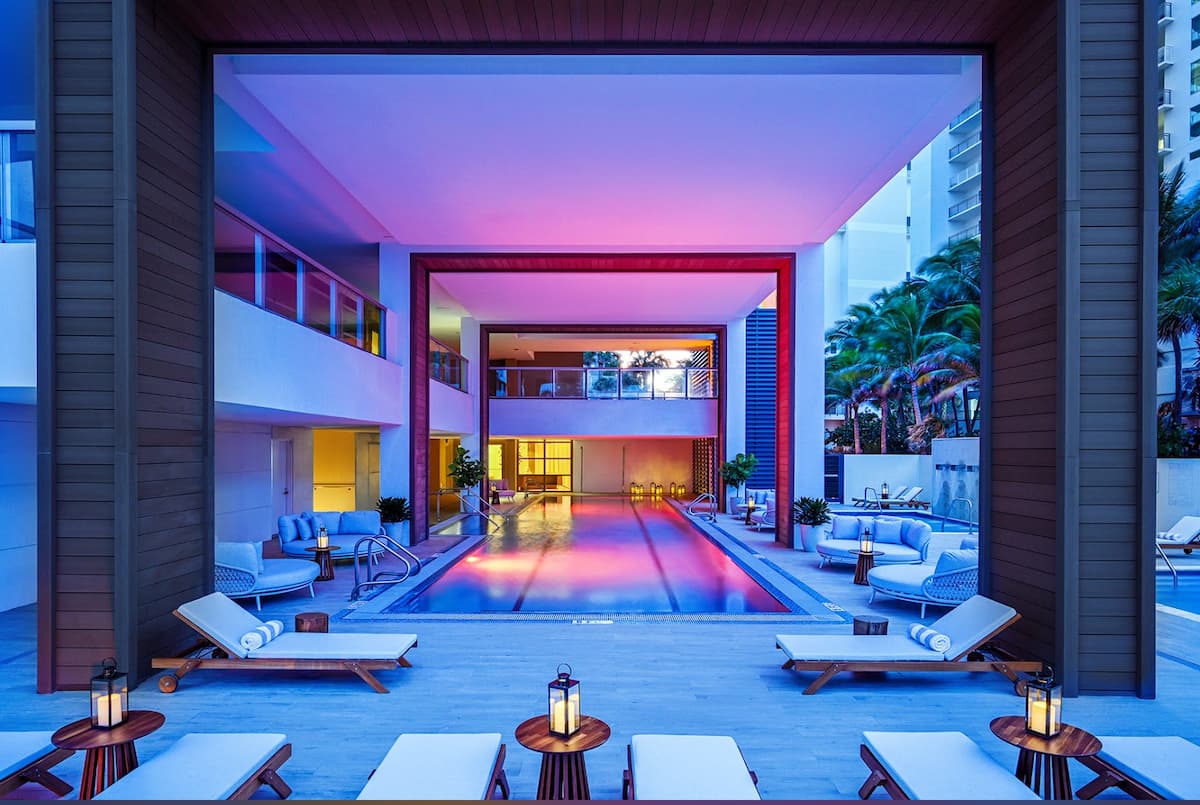 The pool deck after dark, lit in warm and magenta light between the towers