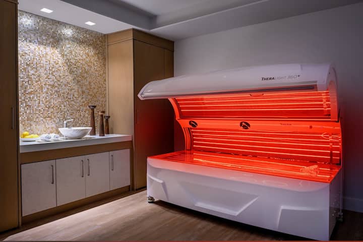 A red-light therapy bed glowing in a private treatment room