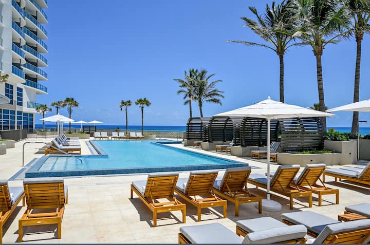 The oceanfront resort pool lined with palms, loungers and umbrellas