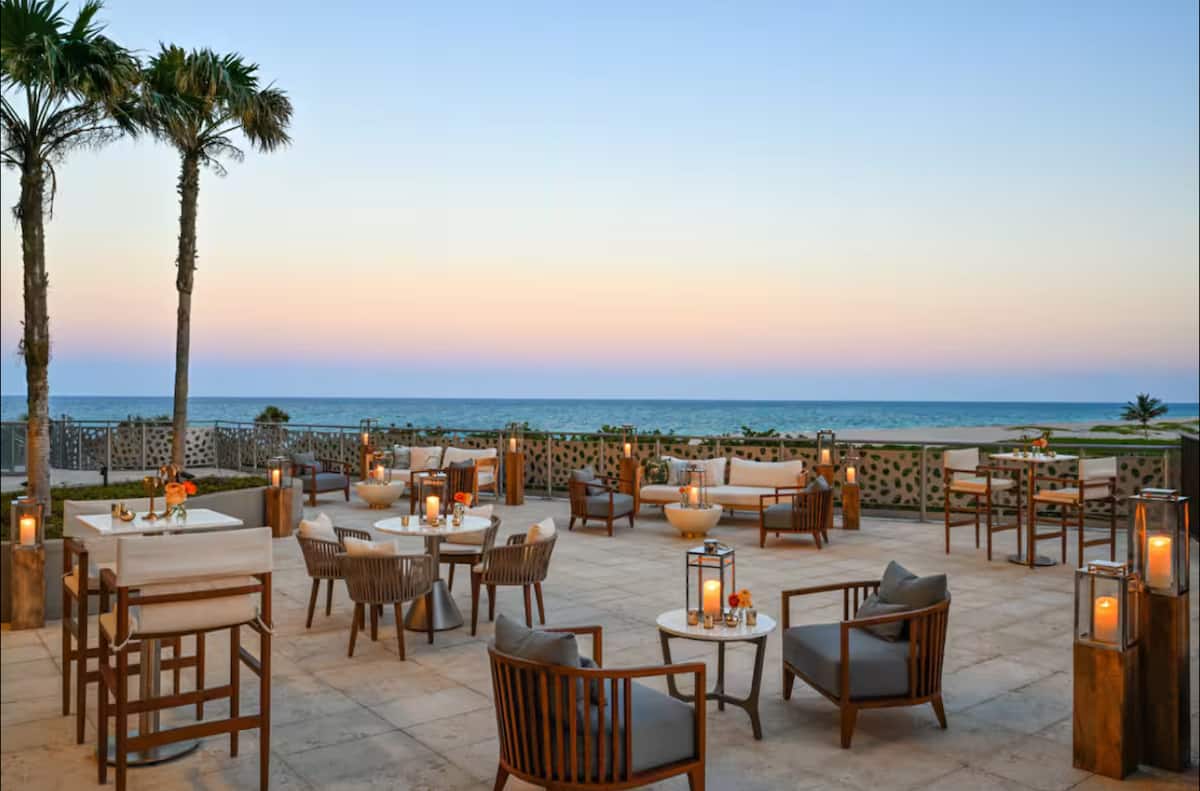 Oceanfront terrace at dusk with lantern-lit tables under palms