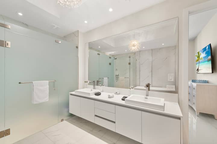 The primary bathroom's long double vanity with lit mirrors and the glass shower behind