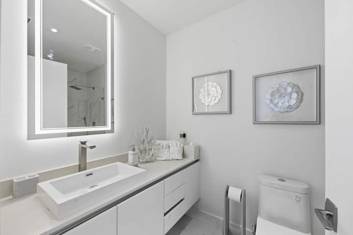 The second bathroom's floating vanity with a lit mirror and framed shell artwork