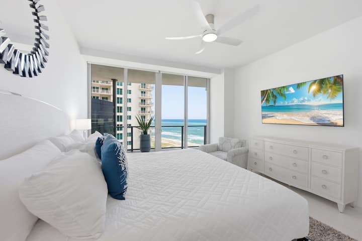 A bedroom dressed in white and blue with a coastal view