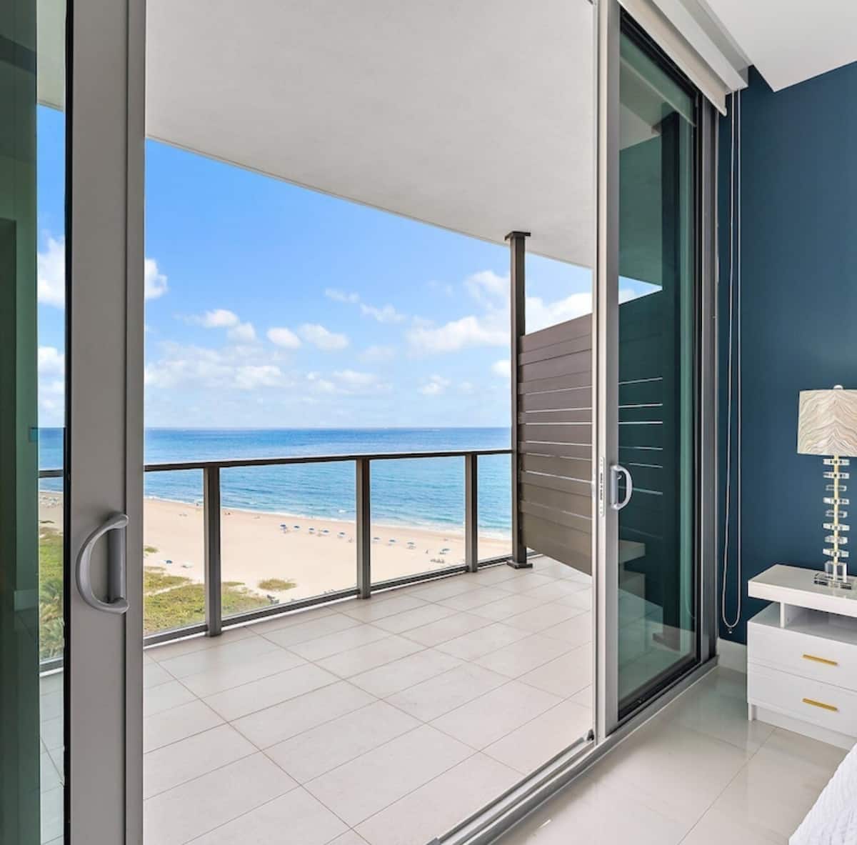 Queen suite with the balcony door open to a wide view of the ocean and beach below