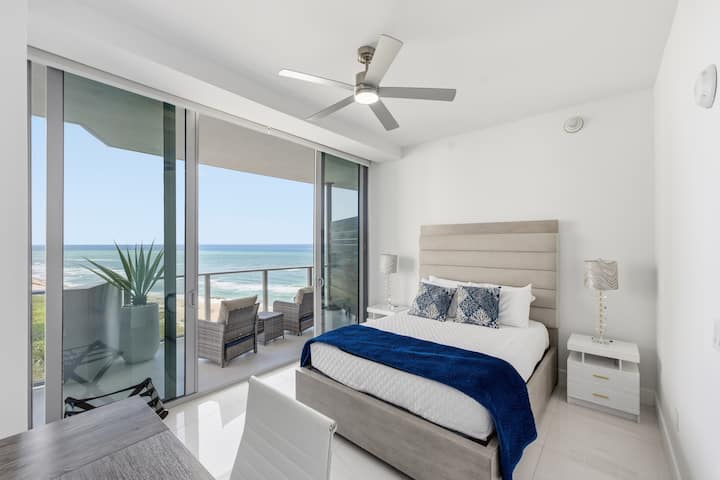 The queen bedroom with a navy throw, a ceiling fan and sliding doors to the balcony and ocean
