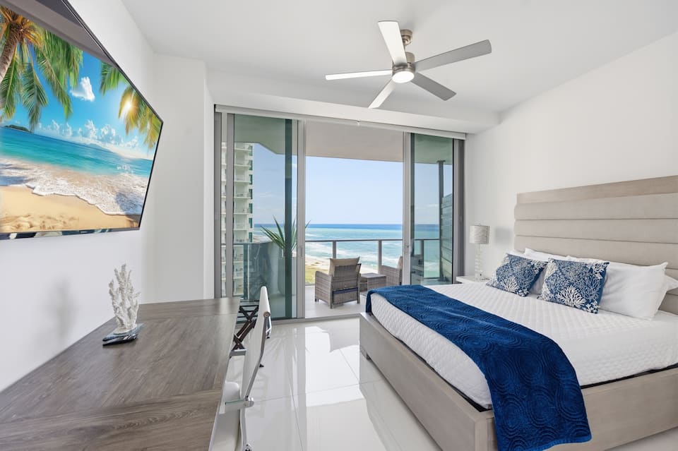 The queen bedroom with a wall-mounted television, ceiling fan and the ocean through the glass
