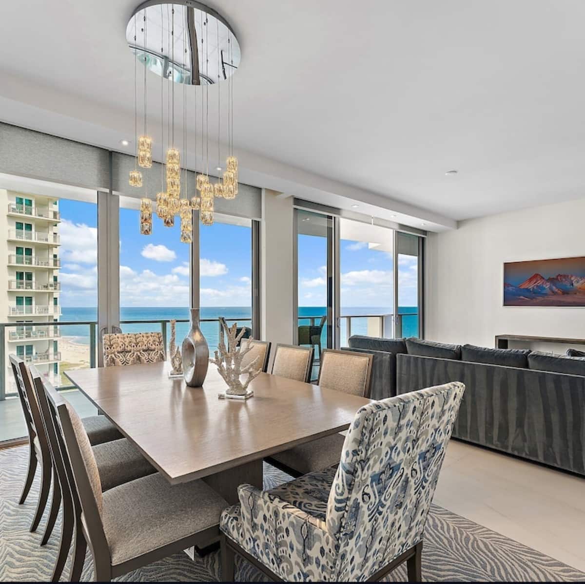 Dining table for eight beneath a cascading glass chandelier, with the ocean filling the windows