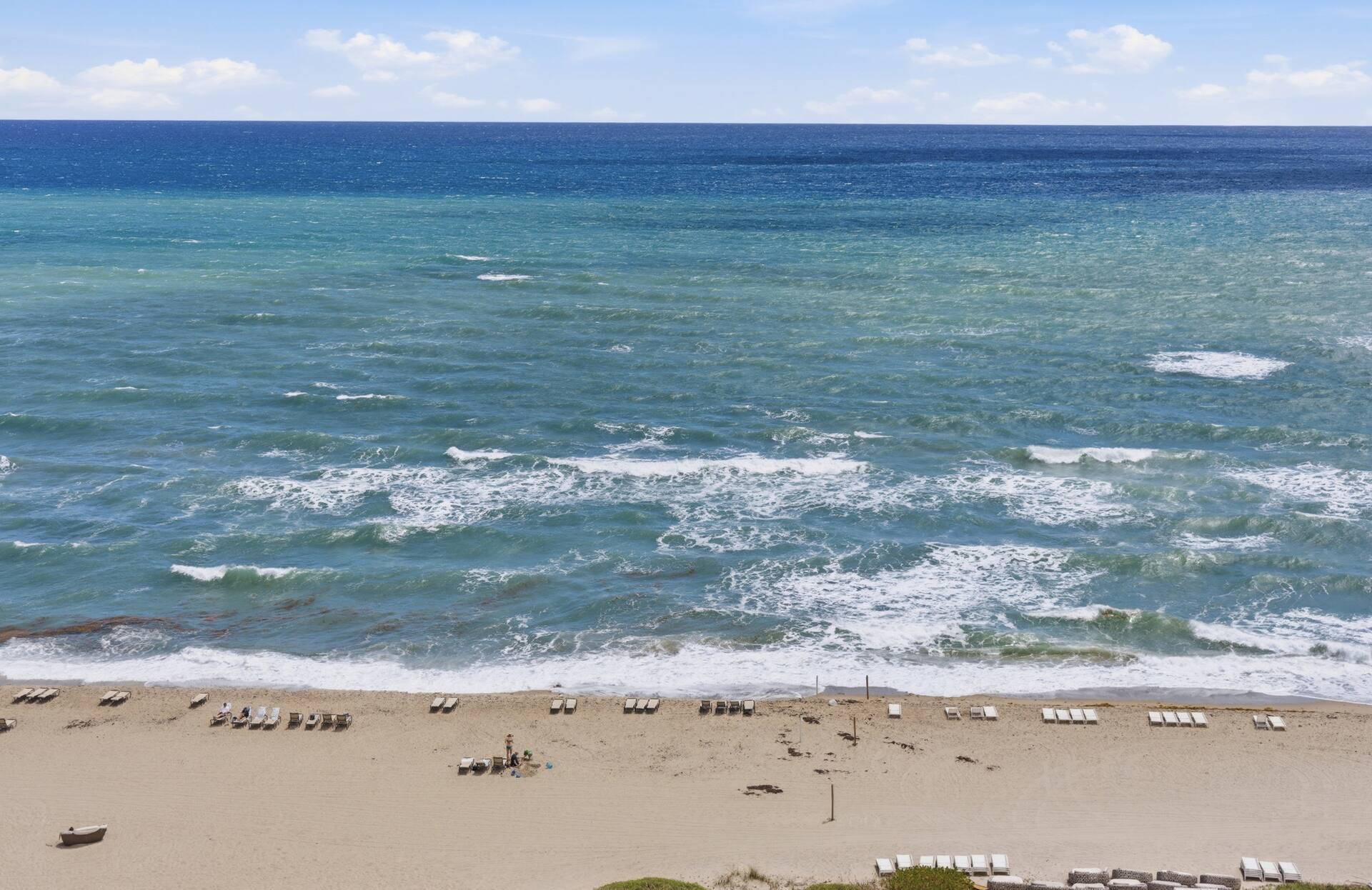 The surf line seen from twelve floors up — sand, loungers and turquoise water