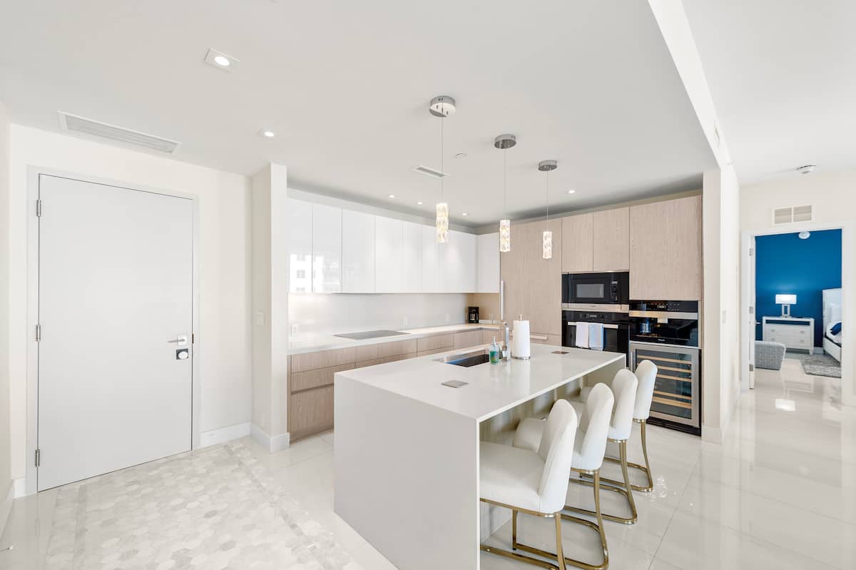 The kitchen island with bar stools, white cabinetry and the built-in coffee machine
