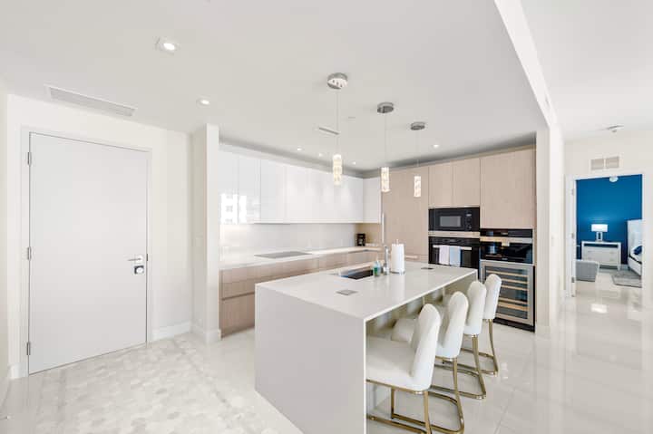 The kitchen island with bar stools, white cabinetry and the built-in coffee machine