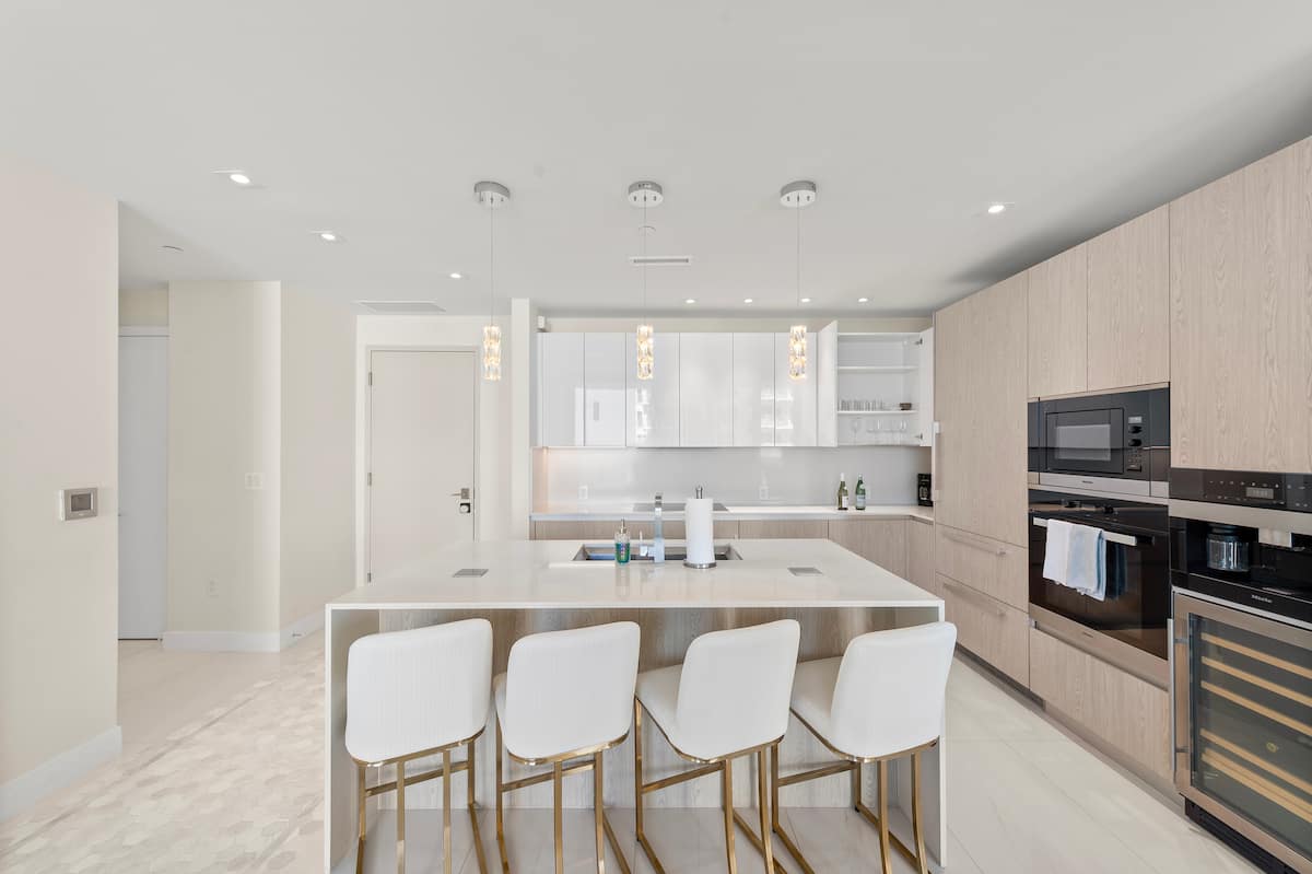 White open-plan kitchen with a long island, four bar stools and pendant lighting