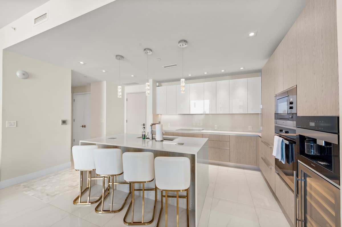 The kitchen island and bar stools facing the wall ovens and coffee machine