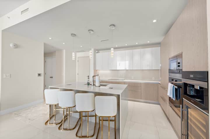 The kitchen island and bar stools facing the wall ovens and coffee machine
