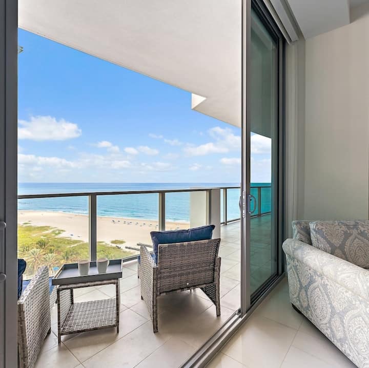 Looking through the open sliding door from the living room to the balcony chairs and the beach below